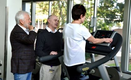 Two people stand next to a person walking on a treadmill